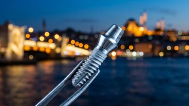 Een close-up van een glanzend titanium tandimplantaat dat wordt vastgehouden door een chirurgische pincet, met op de achtergrond een prachtig onscherp en verlicht stadsbeeld van Istanbul bij schemering.