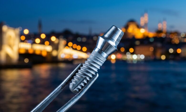Een close-up van een glanzend titanium tandimplantaat dat wordt vastgehouden door een chirurgische pincet, met op de achtergrond een prachtig onscherp en verlicht stadsbeeld van Istanbul bij schemering.