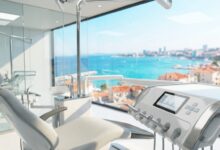 Een interieur van een luxueuze en moderne tandartspraktijk met geavanceerde apparatuur op de voorgrond. Door een groot raam is een zonnig, onscherp uitzicht op een Turkse kuststad te zien, wat het concept van tandheelkundig toerisme illustreert.