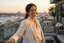 Een gelukkige vrouw met een perfecte, witte glimlach staat op een balkon met een wazig, sfeervol uitzicht op de skyline van Istanbul tijdens zonsondergang.