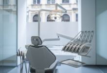 A pristine, high-tech dental clinic with a modern treatment chair and advanced instruments, bathed in cool, bright light. In the soft-focus background, blurred traditional European architecture hints at Belgium.