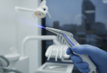 A close-up, photorealistic image of a futuristic dental laser handpiece, emitting a subtle blue light, held by a gloved hand in a sterile dental clinic. A blurred background reveals modern dental equipment and a generic modern European city skyline, suggesting Belgium. The focus is on the precision and advanced technology of laser dentistry.