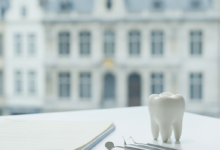 A photorealistic image showing a stack of generic insurance documents next to a clean, minimalist dental model on a modern table. In the blurred background, a classic Belgian architectural building suggests the location. The scene represents healthcare finance and dental reimbursement.