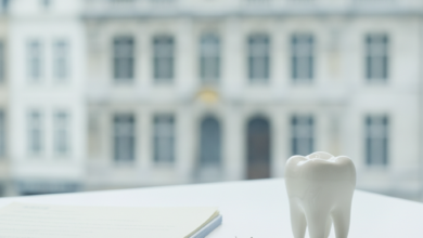 A photorealistic image showing a stack of generic insurance documents next to a clean, minimalist dental model on a modern table. In the blurred background, a classic Belgian architectural building suggests the location. The scene represents healthcare finance and dental reimbursement.
