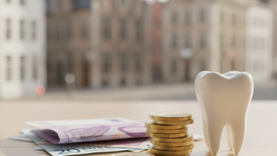 A close-up, photorealistic image of a healthy molar tooth resting on a small stack of Euro coins and next to several Euro banknotes. The background features a softly blurred European cityscape, suggestive of Belgium.