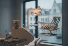 A clean, modern dental examination room with a state-of-the-art dental chair, sleek instruments on a sterile tray, and a blurred background subtly showing European architecture, conveying comfort and advanced dental care.
