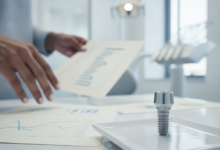 A close-up, photorealistic view inside a modern dental clinic. A stylized model of a dental implant sits on a sterile surface in the foreground. In the soft-focus background, hands are seen reviewing abstract, blurred financial documents, representing the intersection of dental care and insurance costs.