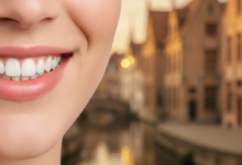 Close-up of a healthy, bright smile with pristine teeth, set against a softly blurred background featuring the characteristic canal-side historic buildings and quaint streets of Bruges, Belgium.